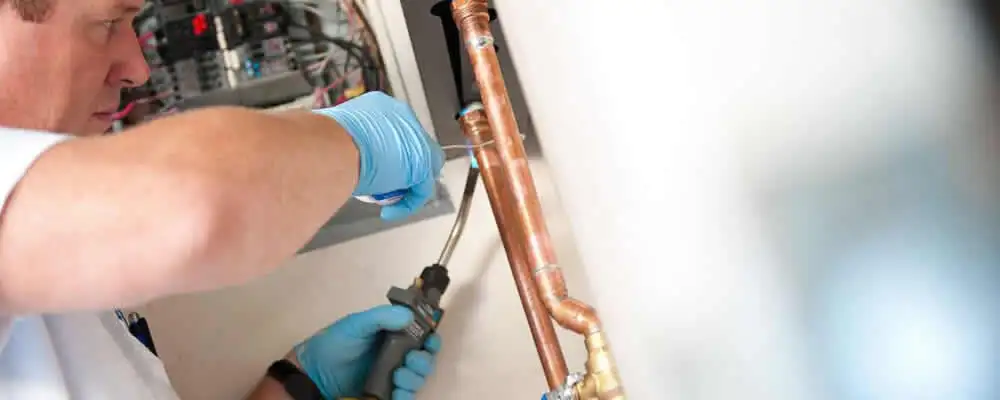 Water heater repair technician testing copper pipe connections and controls in Phoenix, AZ